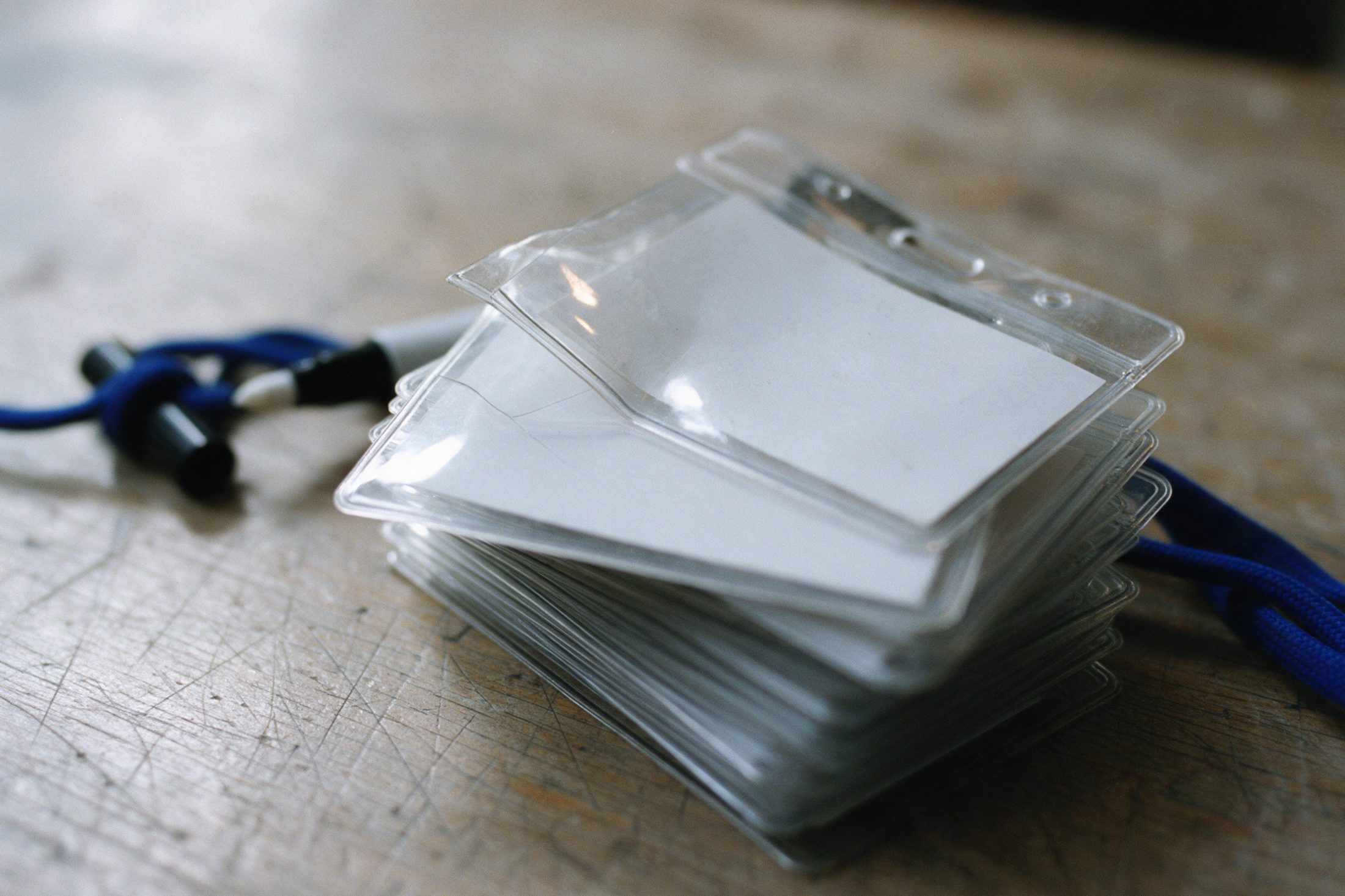 A stack of empty clear badge holders on a scratched table, a blue lanyard cord lying beside them.