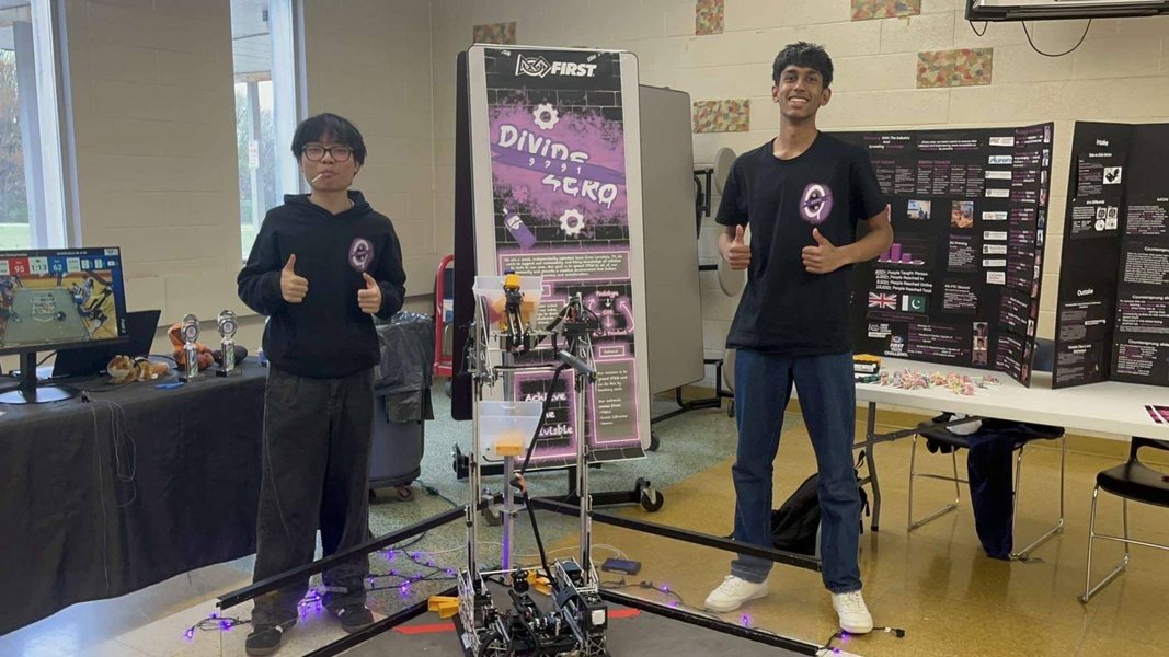 Two students in team shirts giving a thumbs up beside their competition robot at a FIRST Tech Challenge event